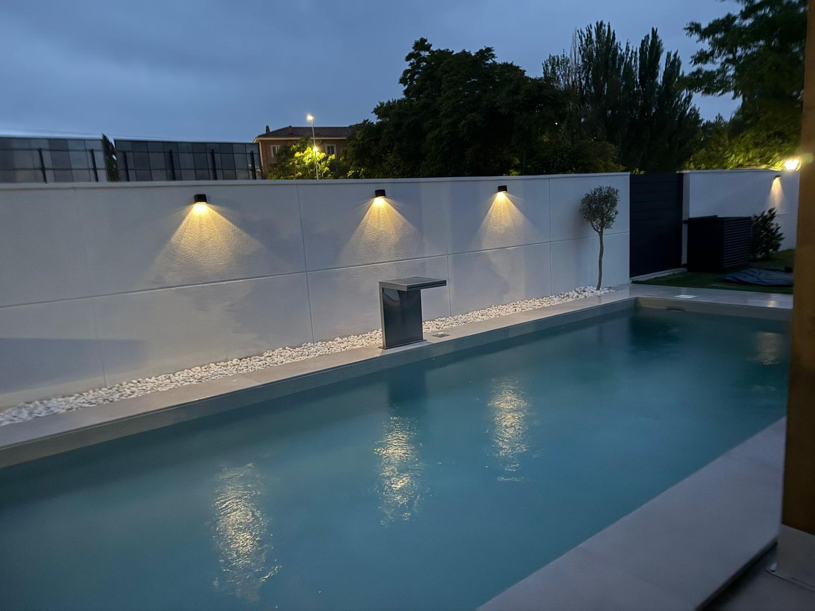 Piscina con muro blanco iluminado y lámina de agua al anochecer