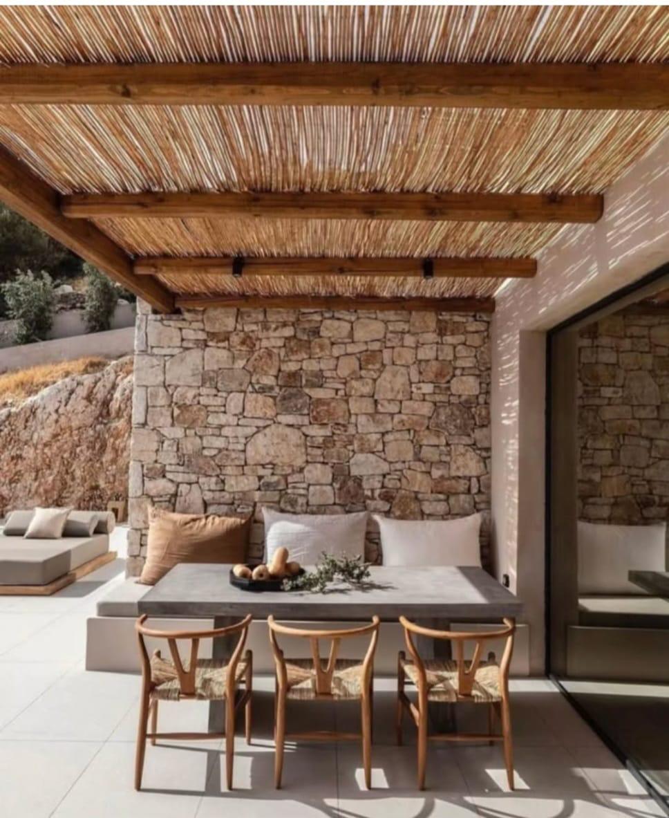 Comedor exterior con muro de piedra natural y pérgola de cañizo